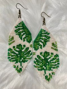 a pair of green and white beaded earrings on top of a white furnish