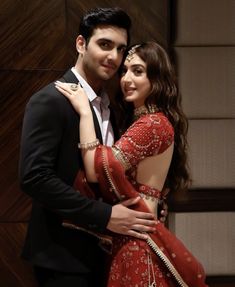 a man in a tuxedo hugging a woman wearing a red dress and headpiece