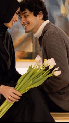 a man and woman sitting on a bench with tulips in front of them