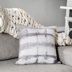 a gray and white pillow sitting on top of a couch next to a knitted blanket