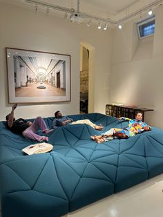 three people laying on top of a blue couch in a room with white flooring