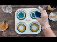 a person in white gloves is making cupcakes with blue and yellow icing