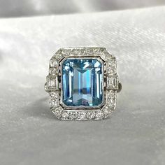 A magnificent gemstone ring featuring a beautiful 5.30-carat emerald cut aquamarine set in bezel. A geometric halo of round-cut diamonds surrounds the center stone. The gemstone are framed by two baguette-cut diamonds that are set in a bezel. The total weight of the diamonds on this ring is approx 1.04 carats. There is an openwork under-gallery on this platinum mounting. ✦ GEMSTONE SPECIFICATIONS: Center Stone: Aquamarine Center Stone Weight: Approx 5.30 Carats Center Stone Cut: Emerald Cut ✦ EN Luxury Aquamarine Octagon Ring, Luxury Emerald Cut Topaz Wedding Ring, Elegant Gia Certified Blue Topaz Diamond Ring, Luxury Octagon Aquamarine Ring, Luxury White Gold Octagon Topaz Ring, Luxury Gia-certified Emerald Cut Topaz Ring, Luxury Octagon Brilliant Cut Topaz Ring, Luxury White Gold Topaz Ring Emerald Cut, Exquisite Emerald Cut Platinum Emerald Ring