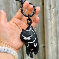 a hand holding a black and white cat keychain with beads on the wrist