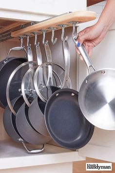 a person is holding pots and pans in a kitchen cabinet with the door open