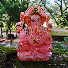 an elephant statue sitting on top of a moss covered rock in front of some trees