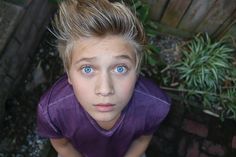 a young boy with blonde hair and blue eyes is looking up at the camera while wearing a purple shirt