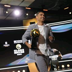 a man holding a golden ball in his right hand and wearing a suit on stage