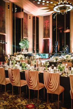 a banquet hall with tables and chairs covered in pink cloths, candles and flowers