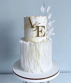 a wedding cake with white icing and gold letters on the top is sitting on a stand