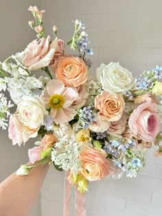 a bouquet of flowers is being held up by someone's hand in front of a brick wall