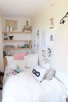 a bed with white sheets and pillows in a bedroom next to shelves on the wall