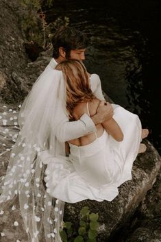 a bride and groom are sitting on rocks by the water