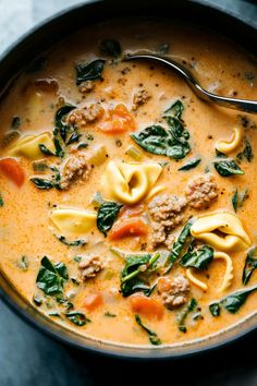 a bowl filled with pasta, meat and spinach in broth next to a spoon