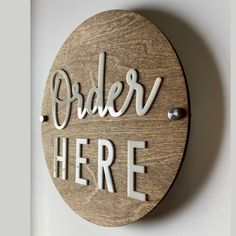 a wooden sign that says order here on the side of a wall with white lettering