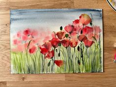 a watercolor painting of red poppies on a wooden table next to a brush