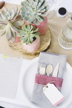 a place setting with succulents and paper napkins on the table for two