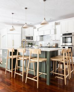 a kitchen with white cabinets and wooden flooring has stools around the island counter