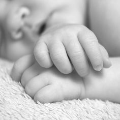 a black and white photo of a baby's hand on top of a blanket