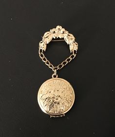 "Lovely vintage signed Monet hanging/dangling gold-tone brooch with impressed intricate floral design on the front and back of the locket, which hangs from a chain connected to a flower-and-leaf arch. (Any darker areas are reflections of us taking the photo! The pin has a polished finish.) The pin is in excellent condition and measures approx. 1.25\" across (arched pin at the top; the locket is 1\" across) and is 2.75\" long with the locket closed. See photo 3 to see the open locket; the hinge is at the base and the locket opens downward. This piece is as beautiful to wear as it would be in a collection.  We do our best to describe each selection and welcome any questions you may have. Pictures are also part of the description, so please look them over and read the entire description. Chec Victorian Gold Brooch With Locket, Victorian Gold Locket Brooches, Ornate Gold Locket Brooches, Gold Locket Brooch For Collectors, Antique Gold Medallion Brooch, Gold Locket-shaped Brooch, Ornate Gold Medallion Brooches, Gold Brooches With Vintage Charm As Gift, Gold Brooches With Vintage Charm For Gift