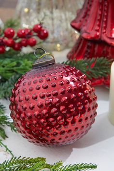 a red ornament sitting on top of a table next to candles and greenery