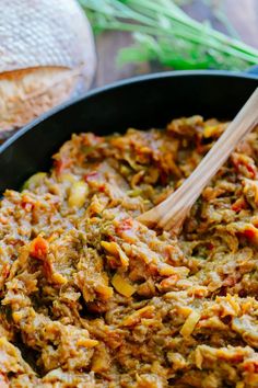 a pan filled with meat and vegetables on top of a wooden table next to bread