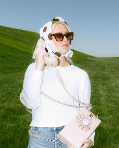 a woman in sunglasses is holding a cell phone and wearing a cow print scarf over her head