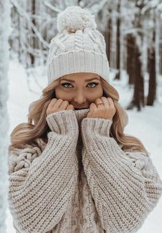 a woman wearing a white hat and sweater in the snow with her hands on her face