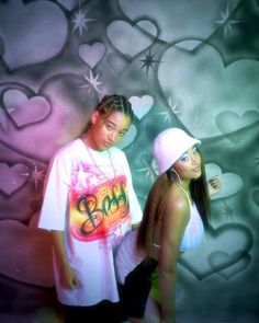 two young women standing next to each other in front of a wall with hearts on it