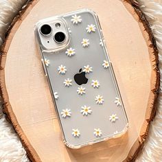 an iphone case with daisies on it sitting on top of a wooden slice in front of a white background