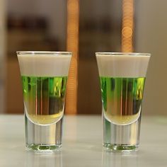 two shot glasses filled with green liquid sitting on a white counter top next to each other