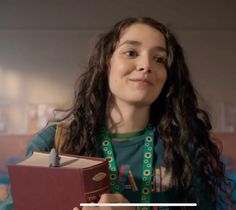 a girl with long curly hair is holding a book and looking up at the camera