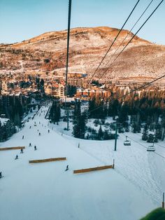 skiers are skiing down a snowy hill near a ski lift in the background is a town