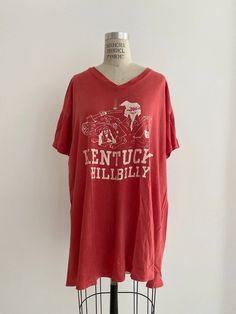 ITEM DESCRIPTION 70s Vintage, Kentucky Hillbilly V-neck shirt. Single Stitch. Brand : Vintage - Unknown Size : Unknown Color : Red MEASUREMENTS Shoulder to shoulder : 22 Bust (armpit to armpit) : 25 Back length : 30 "Worn well natural distressed, cople small holes and ripping side hem, see attached pics, as is condition." Retro V-neck T-shirt For Spring, Vintage V-neck T-shirt For Spring, Vintage V-neck Top With Relaxed Fit, Vintage Cotton V-neck Top, Retro V-neck Relaxed Fit Top, Vintage V-neck T-shirt With Graphic Print, Vintage Distressed Tops For Spring, Vintage Distressed Tops For Fall, Casual Distressed V-neck Top