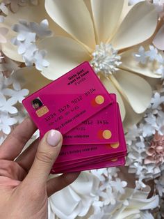 a hand holding three pink credit cards in front of flowers