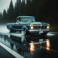 an old blue truck driving down the road at night with fog and trees in the background