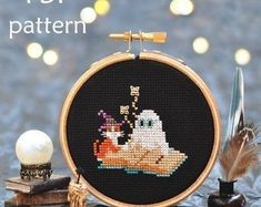 the cross stitch pattern is on display next to some books and an object with feathers