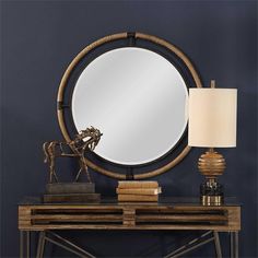 a round mirror sitting on top of a wooden table next to a lamp and books