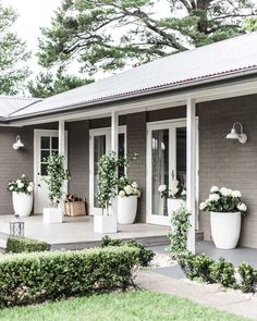 two large white planters sitting on the front porch of a gray house with windows