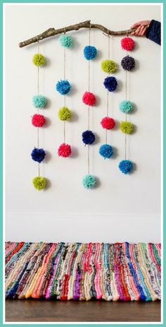 a colorful wall hanging with pom - poms on it and a hand holding a branch