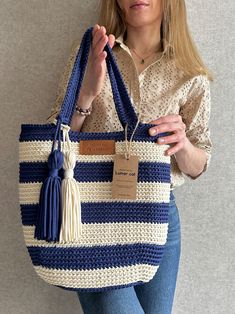 a woman holding a blue and white striped bag with tassels on the handles