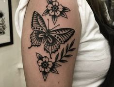 a black and white butterfly tattoo on the left upper half of the arm, with flowers around it