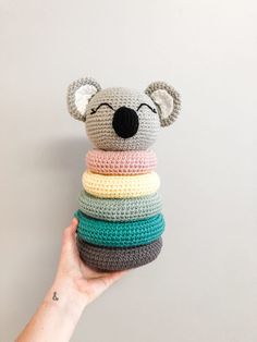 a crocheted koala bear sitting on top of a stack of multicolored pillows