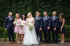 a group of people standing next to each other in front of a green plant wall