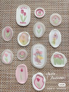 some pink and white buttons with flowers on them sitting next to each other in front of a burlap background