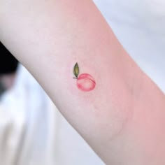 a small apple tattoo on the left arm and wrist area, with a green leaf sticking out of it