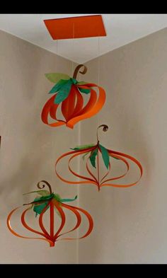 three paper pumpkins hanging from the ceiling in a room with white walls and orange accents