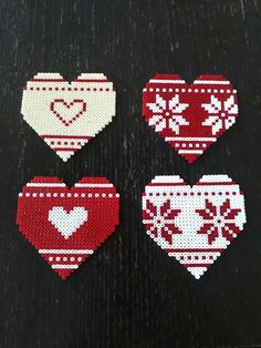 three heart shaped cross stitch ornaments on a black tablecloth with red and white designs