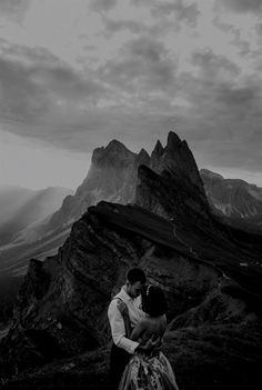 a man and woman embracing on top of a mountain with mountains in the back ground