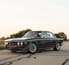 an old black bmw is parked on the side of the road